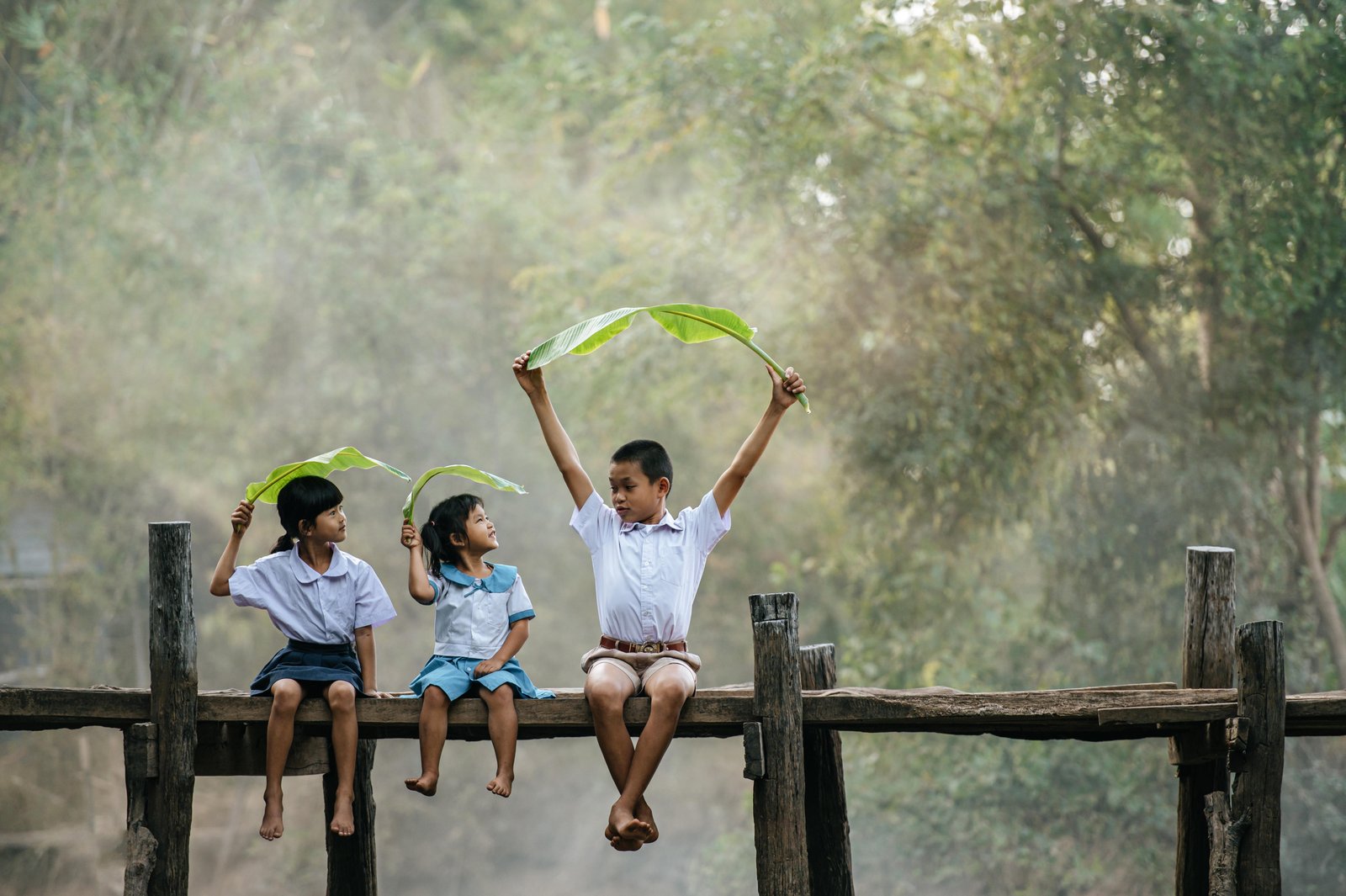 asian-boy-little-girls-sitting-wooden-bridge-joyful-playing-with-banana-leaves-head-smile-laughting-with-funny-together-copy-space-rural-scene-style-concept