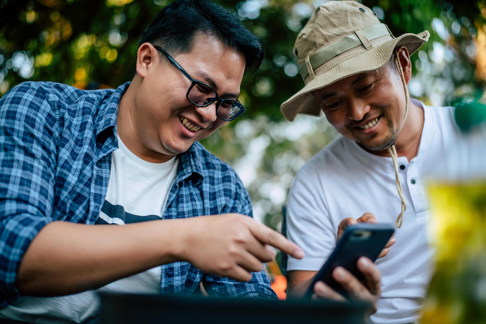 portrait-happy-asian-man-friends-sitting-chair-camp-with-talking-looking-smartphone-cooking-set-front-ground-outdoor-cooking-traveling-camping-lifestyle-concept