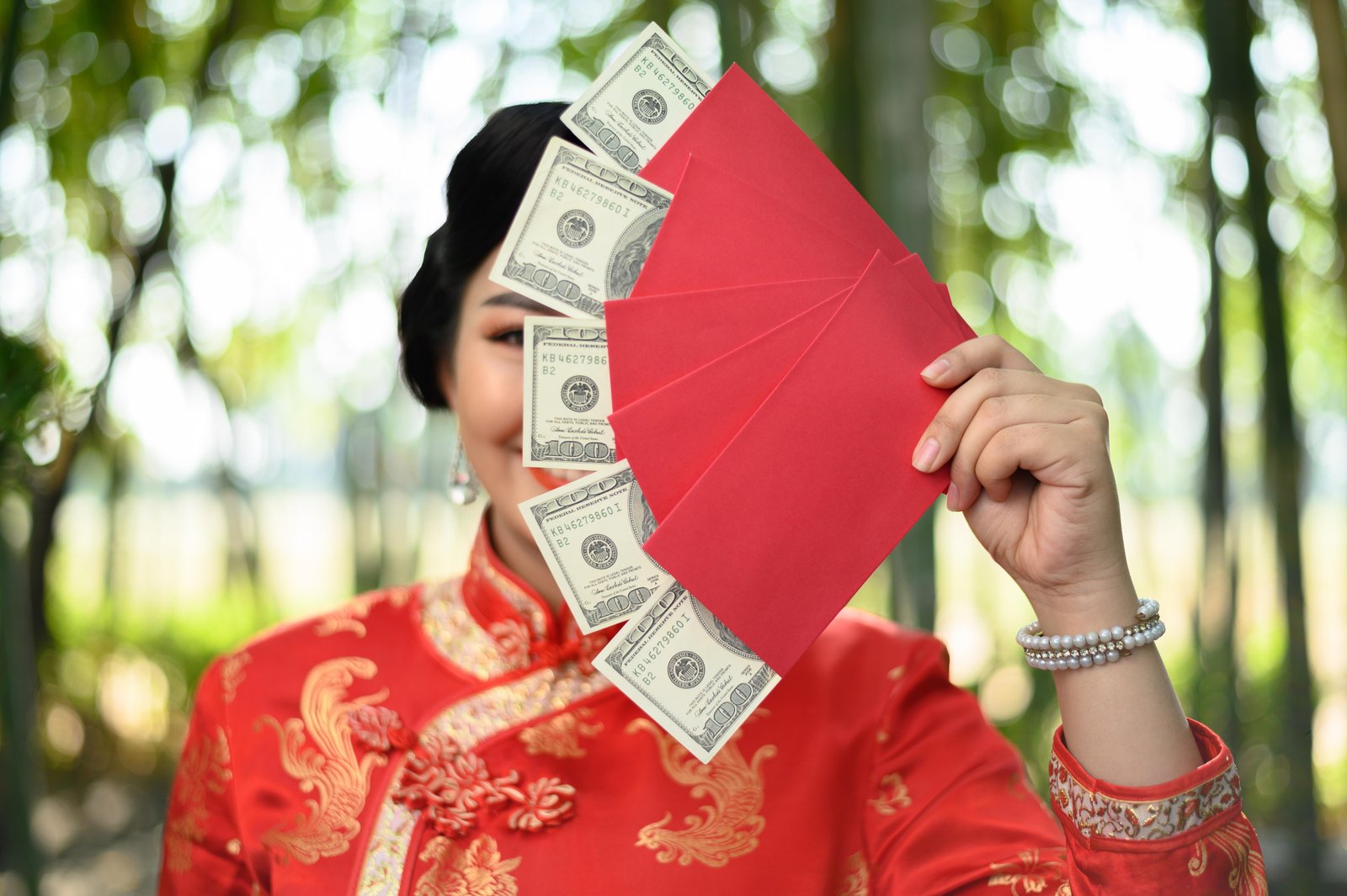 selective-focus-pretty-asian-woman-chinese-cheongsam-holding-envelopes-dollars-banknote-fan-hidden-eye-bamboo-forest
