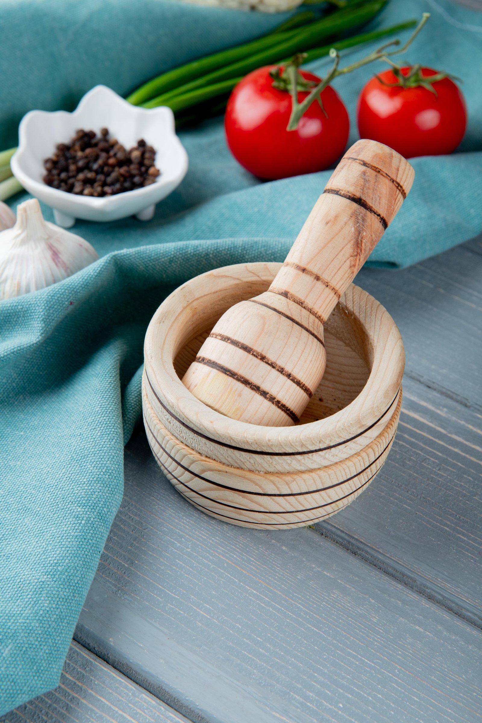 side-view-garlic-crusher-with-vegetables-black-pepper-blue-cloth-surface-wooden-background