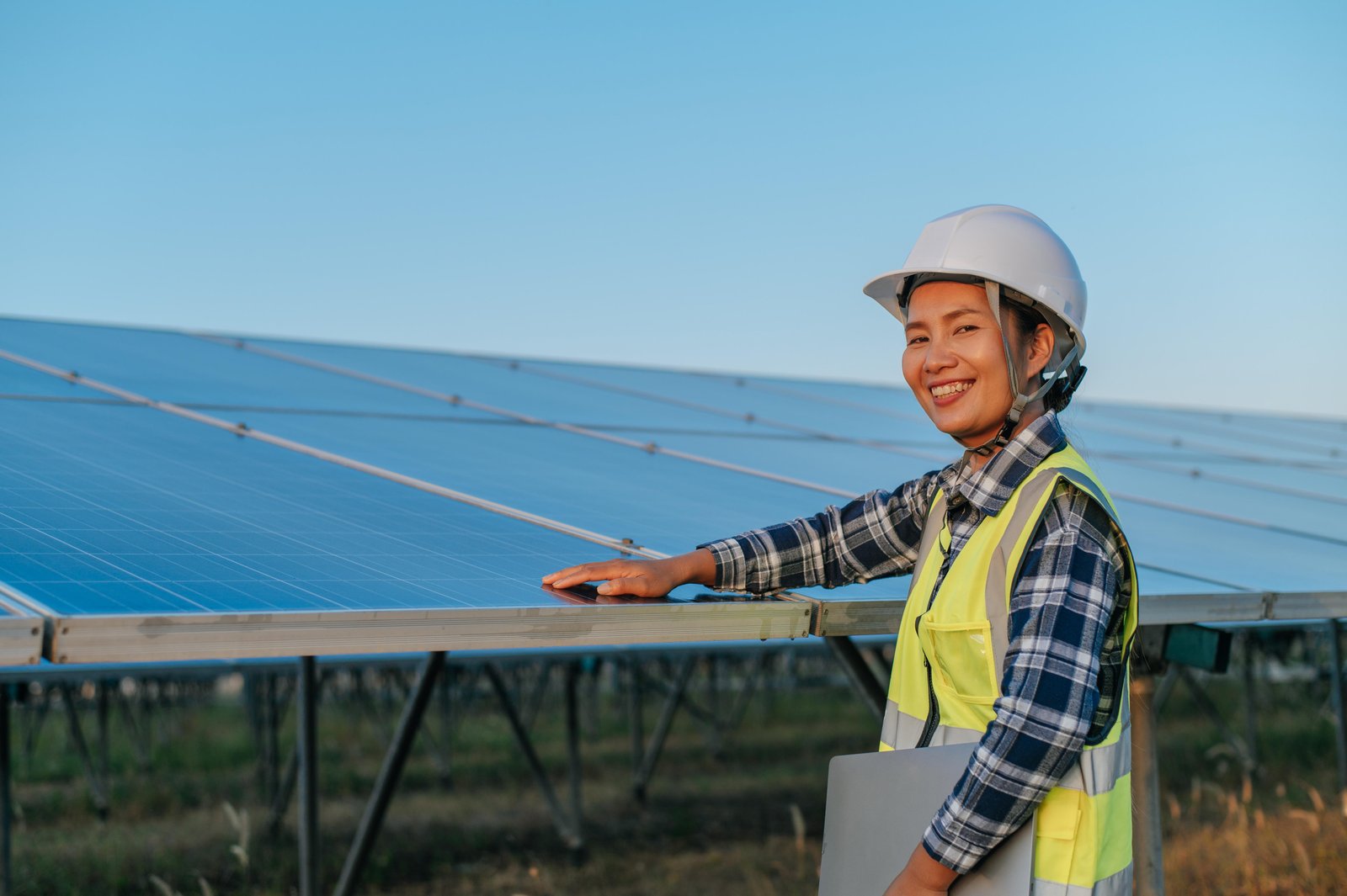 young-asian-female-inspector-engineer-touching-checking-operation-photovoltaic-solar-panel-outdoor-station-holding-laptop-computer-looking-camera-with-smile-copy-space