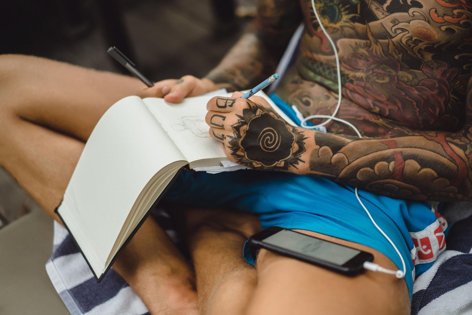 young-man-tattoos-wearing-headphones-listens-music-draws-notebook